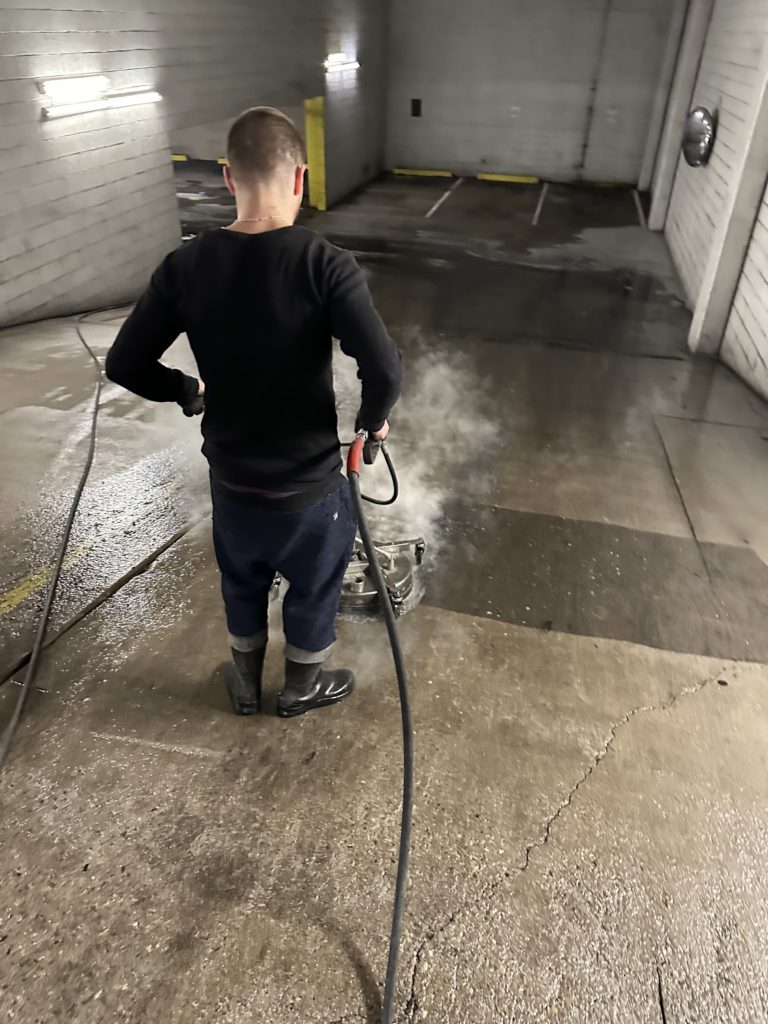 JP's Junk Removal team member power washing the slanted floor of a parking garage
